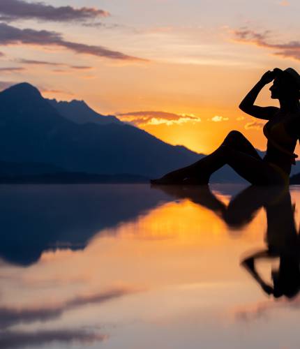 Frau sitzt bei Sonnenuntergang am Infinity Pool