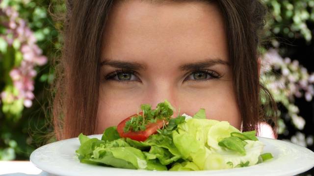 Frau hält sich Salatteller ins Gesicht